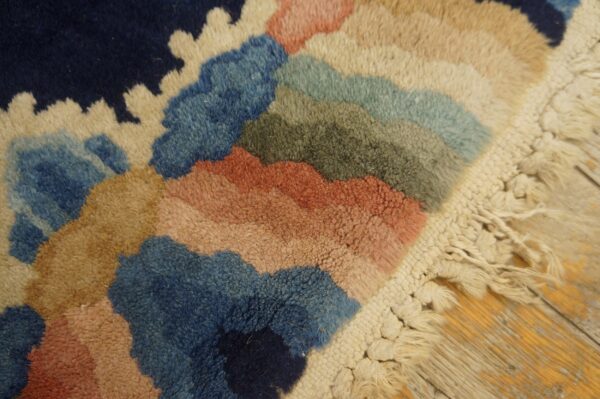Plush rug edge showing abstract shapes in navy, blue, rust, and tan with thick cream fringe.
