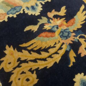 A plush navy rug displays a stylized yellow and coral bird motif on wooden flooring.