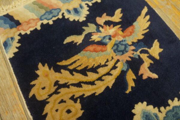 A plush navy rug displays a stylized yellow and coral bird motif on wooden flooring.