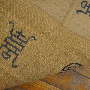 A textured gold and blue patterned rug is folded over, showing its weave on worn wood flooring.