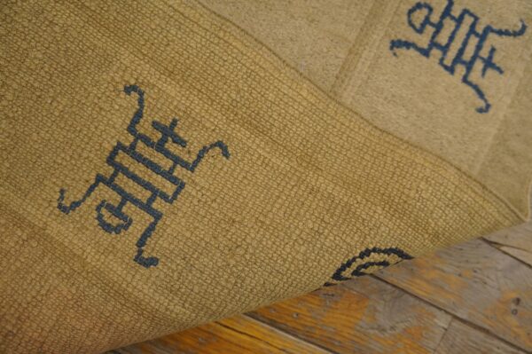 A textured gold and blue patterned rug is folded over, showing its weave on worn wood flooring.
