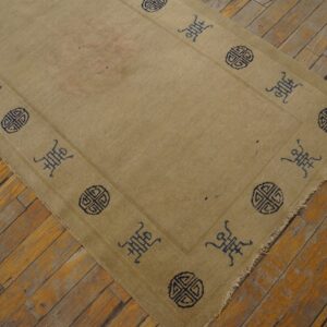 Low-pile tan rug featuring dark symbolic patterns along the border on distressed wood floors.
