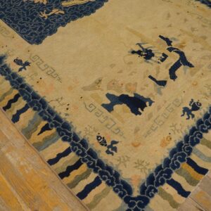 Low-pile tan and navy rug featuring stylized motifs and geometric borders on distressed wood planks.