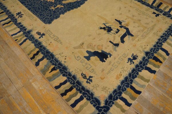 Low-pile tan and navy rug featuring stylized motifs and geometric borders on distressed wood planks.