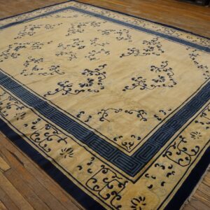 A large beige and blue patterned rug with elaborate borders covers distressed wooden floorboards.