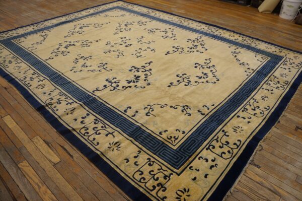 A large beige and blue patterned rug with elaborate borders covers distressed wooden floorboards.