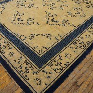 A large gold rug with navy blue floral and geometric key borders rests on distressed wood floors.