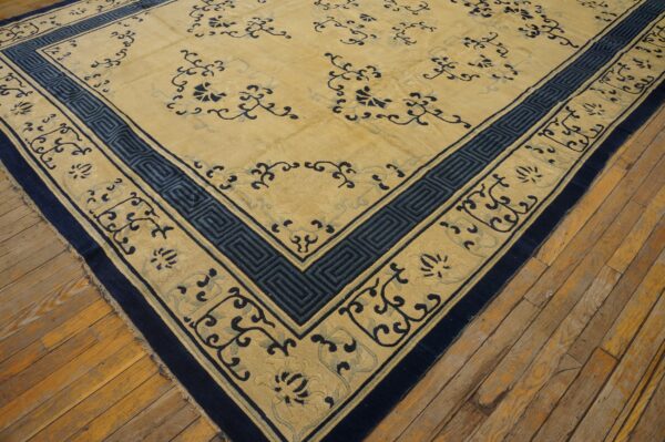 A large gold rug with navy blue floral and geometric key borders rests on distressed wood floors.