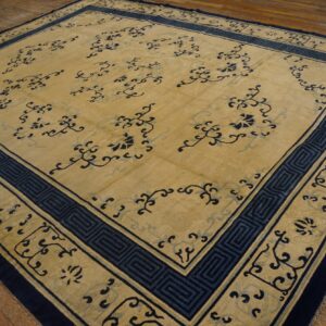 Low-pile tan rug with carved dark blue floral patterns and a geometric border on wood flooring.