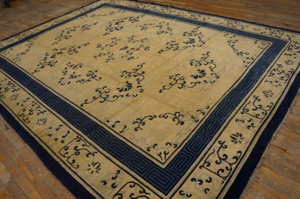 Low-pile tan rug with carved dark blue floral patterns and a geometric border on wood flooring.