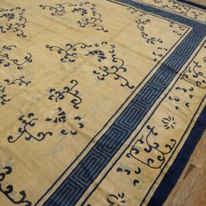 Pale yellow rug with deep blue meandering border and scrolling floral patterns on wood planks.