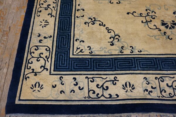 Tan and navy patterned rug featuring geometric borders and floral motifs on aged wood planks.