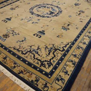 Tan rug with navy blue borders and stylized floral patterns, including a medallion, resting on wood floorboards.