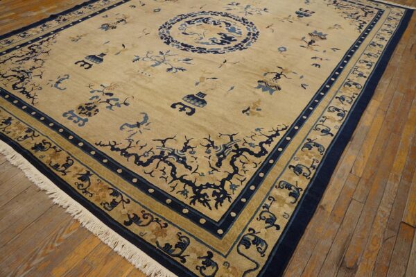 Tan rug with navy blue borders and stylized floral patterns, including a medallion, resting on wood floorboards.