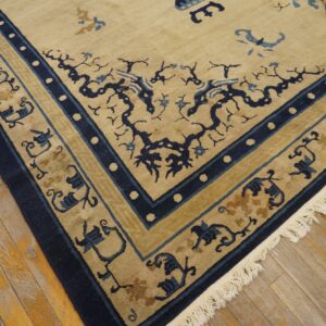 Tan rug with navy and light blue botanical designs and patterned borders rests on distressed wood flooring.