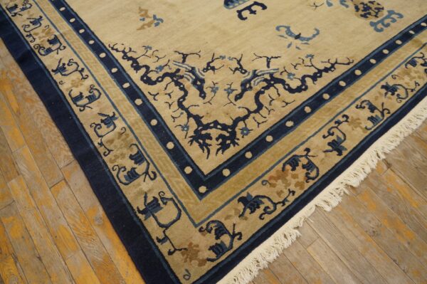 Tan rug with navy and light blue botanical designs and patterned borders rests on distressed wood flooring.