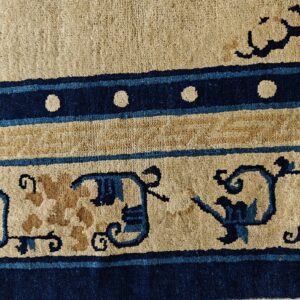 Low-pile rug detail showing cream, tan, and dark blue bands with stylized scroll and circular patterns.