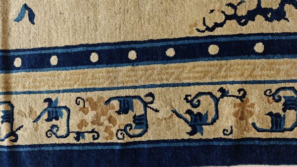 Low-pile rug detail showing cream, tan, and dark blue bands with stylized scroll and circular patterns.