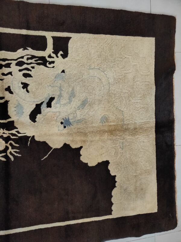 Close-up of a dark brown rug corner with an off-white field featuring stylized blue and gray floral motifs on white tile.