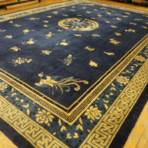 Deep navy blue rug featuring golden yellow stylized floral and geometric border patterns on wood flooring.
