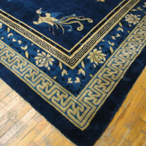 Deep blue rug with golden yellow fret borders and a bird motif rests on light plank wood flooring.