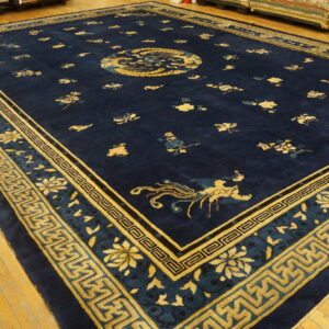 Large navy blue rug featuring gold East Asian motifs and geometric fret borders on wood flooring.