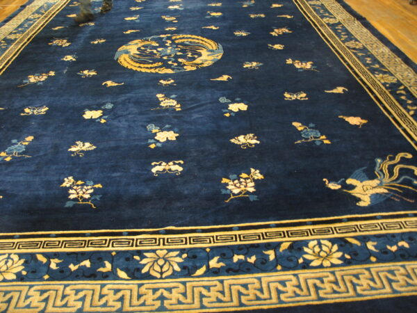 Plush deep blue rug with scattered gold flowers, a central mythical bird motif, and geometric gold borders.