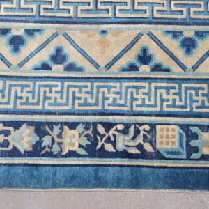 Detailed blue and beige rug borders show Greek key and stylized floral patterns on a gray concrete floor.