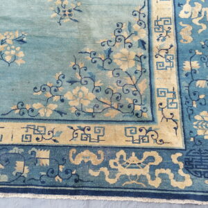 Teal rug corner featuring tan flowers, dark blue vines, and multiple decorative geometric borders.