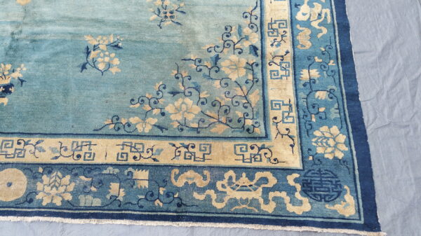 Teal rug corner featuring tan flowers, dark blue vines, and multiple decorative geometric borders.