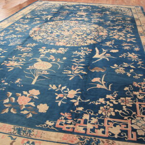 Large blue rug featuring scattered floral patterns, birds, and a central medallion in light beige and pink.