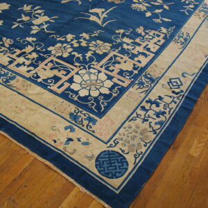 Detailed corner of a blue rug with tan, pink, and light blue floral designs resting on wood plank flooring.