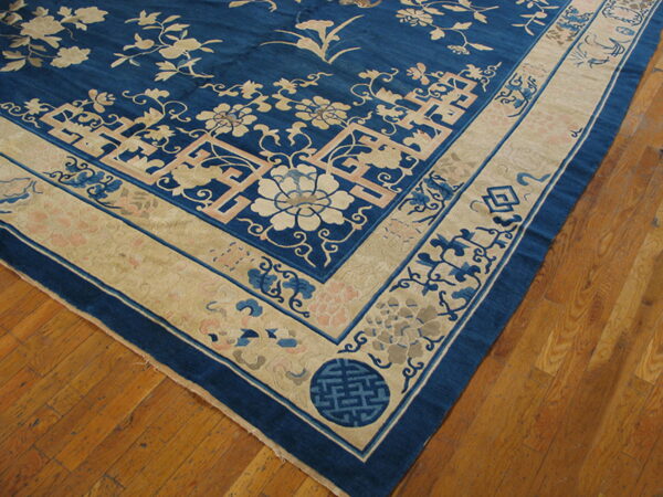 Detailed corner of a blue rug with tan, pink, and light blue floral designs resting on wood plank flooring.