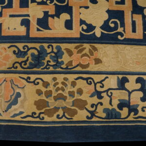Detail of a rug border featuring blue, tan, and coral floral and geometric motifs on a short pile.