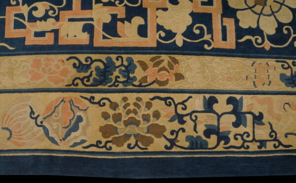 Detail of a rug border featuring blue, tan, and coral floral and geometric motifs on a short pile.