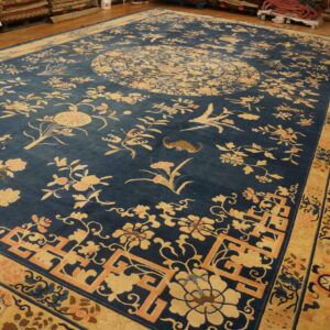 Traditional blue rug with intricate gold floral and bird designs, lying on glossy wood plank flooring.