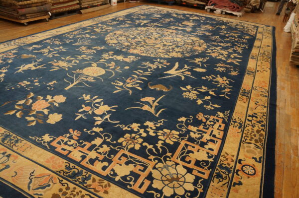 Traditional blue rug with intricate gold floral and bird designs, lying on glossy wood plank flooring.