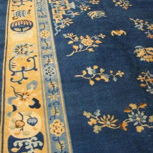 A deep blue rug with gold floral patterns and complex tan borders rests on plank hardwood flooring.