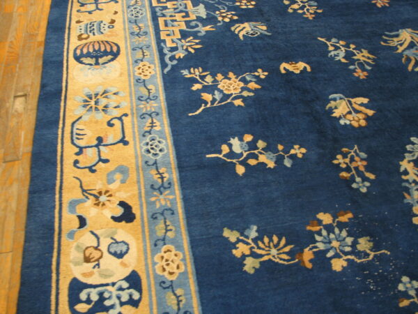 A deep blue rug with gold floral patterns and complex tan borders rests on plank hardwood flooring.