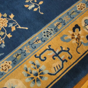 Navy blue rug featuring intricate gold and light blue floral and vine border patterns near wood flooring.
