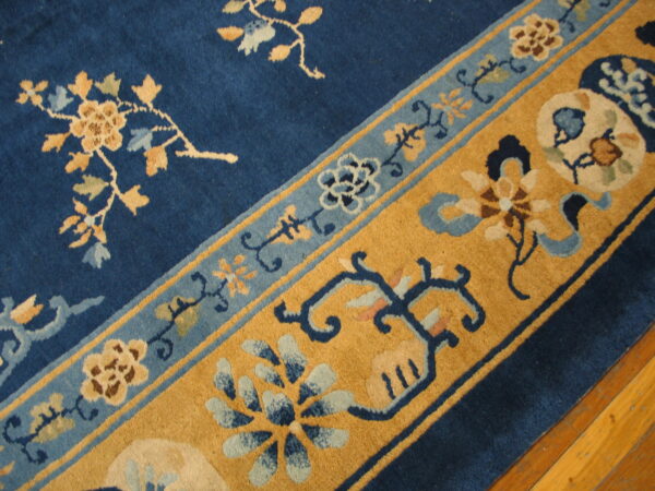 Navy blue rug featuring intricate gold and light blue floral and vine border patterns near wood flooring.