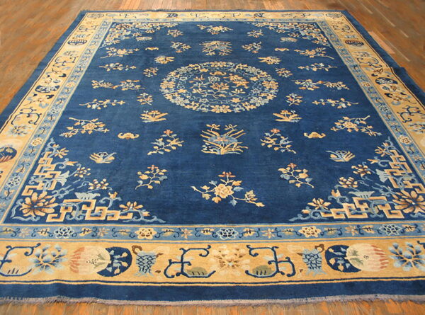 Blue rug with gold and light blue floral patterns and decorative borders covering a wood floor.