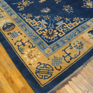 Corner view of a blue and gold rug featuring detailed floral and geometric patterns on hardwood flooring.