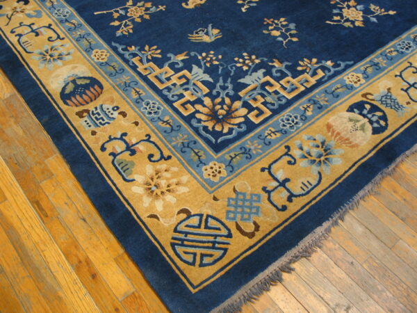 Corner view of a blue and gold rug featuring detailed floral and geometric patterns on hardwood flooring.