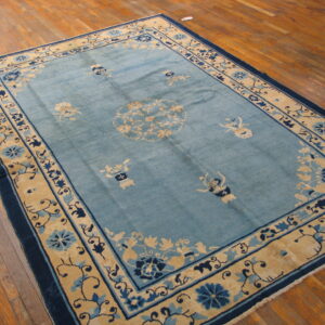 A rectangular teal rug with intricate beige and dark blue floral patterns resting on polished wood floors.
