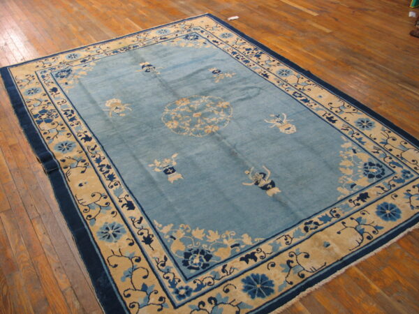 A rectangular teal rug with intricate beige and dark blue floral patterns resting on polished wood floors.