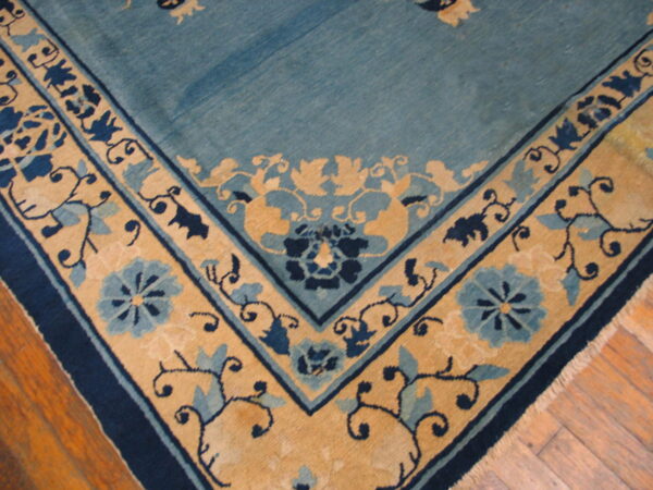 A blue rug with a decorative tan and navy floral border rests on a wooden floor.