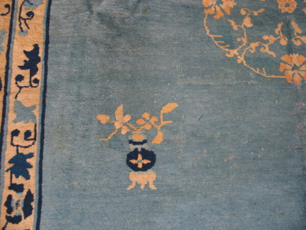 Low-pile blue rug featuring distressed texture, a tan and navy vase pattern, and a patterned border.
