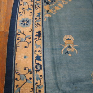 Close-up of a dusty blue rug with tan and navy floral borders placed on warm plank hardwood flooring.