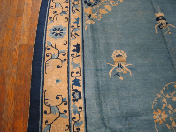 Close-up of a dusty blue rug with tan and navy floral borders placed on warm plank hardwood flooring.